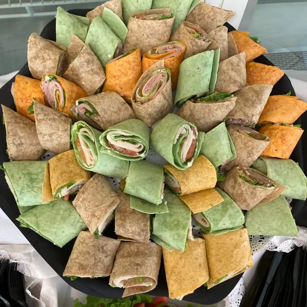 A platter of colorful wraps, some cut in half, revealing fillings of meat, cheese, and lettuce.