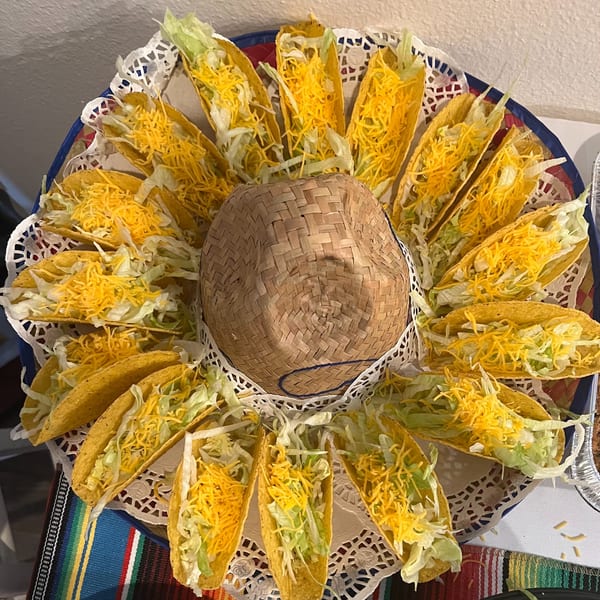 A sombrero-shaped platter of hard-shell tacos filled with shredded lettuce and cheddar cheese.
