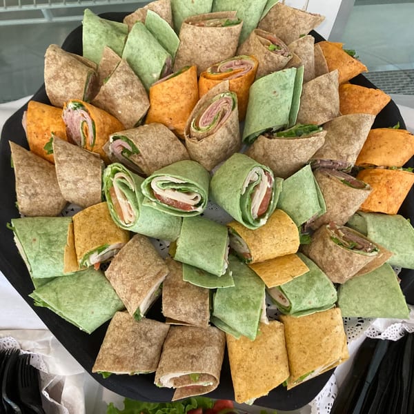 A catering tray filled with various colorful wraps, including green, orange, and whole wheat tortillas.