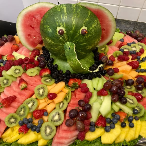 A fruit platter with a watermelon carved into an elephant surrounded by various fresh fruits.