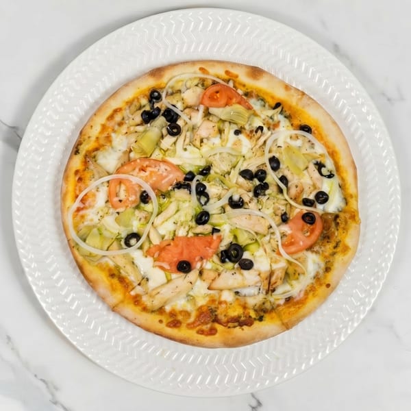 A whole chicken pizza with olives, tomatoes, onions, and artichoke hearts on a white plate.