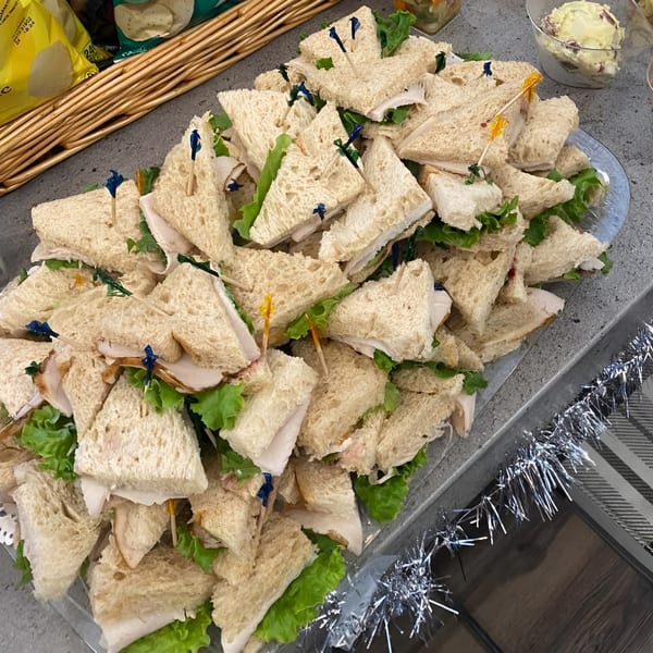 A platter of triangular turkey and lettuce sandwiches with decorative toothpicks, next to a basket of chips.