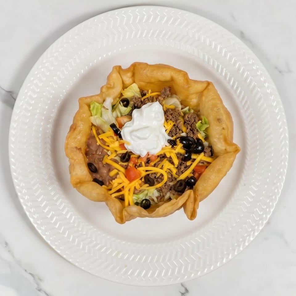 A taco salad in a crispy fried tortilla bowl, topped with sour cream, on a white plate.