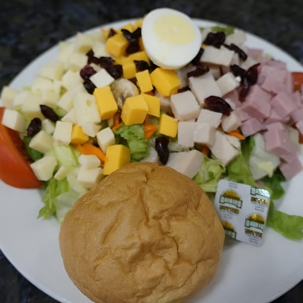 Chef salad with ham, turkey, cheese, egg, and cranberries, served with a dinner roll and butter.